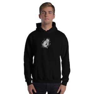 May include: Black hooded sweatshirt featuring a white and grey graphic. The design is an abstract shape with surrounding dots. The sweatshirt has a front pocket and a drawstring hood. The garment is made of a soft material.