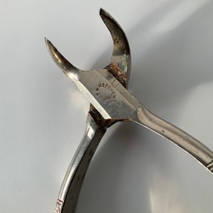 May include: A silver metal tool with a curved handle and a sharp point. The tool is marked with the text "J. Stevens & Co."