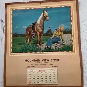 Op de afbeelding: Een vintage kalender met een foto van een vrouw die op een rots zit met een palominopaard. De kalender is voor de Mountain View Store in Alder Flats, Alberta, Canada. De maand is januari 1962.