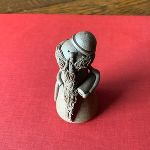 Puede incluir: Una figurita de cerámica de un hombre barbudo con un sombrero. La figurita es de color marrón y tiene una superficie texturizada.