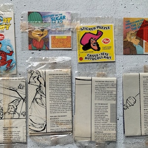Puede incluir: Una colección de ocho tapas de cajas de cereales Post vintage con personajes de dibujos animados populares como Sport Goofy, el Capitán Garfio y el Chico del Panal. Las tapas de las cajas están en bolsas de plástico e incluyen instrucciones para manualidades y actividades.