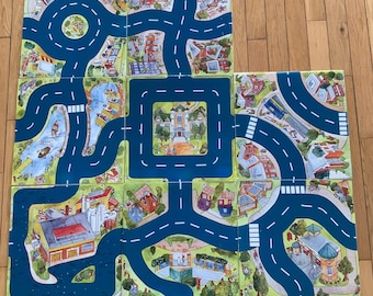 May include: A colorful play mat with a city scene featuring buildings, roads, and trees. The mat is made up of multiple square tiles that can be arranged in different ways. The roads are blue and white, and the buildings are brightly colored.