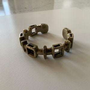 Può includere: Un braccialetto d'argento con un design geometrico. Il braccialetto è composto da più maglie quadrate collegate da un pezzo centrale testurizzato.