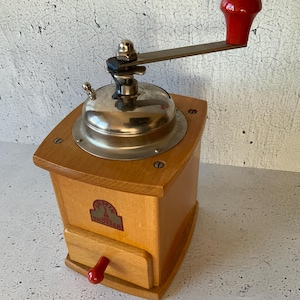 May include: A vintage wooden coffee grinder with a red handle and a drawer. The grinder has a metal top and a label that reads "F.A.T.Z. TROCKEN".