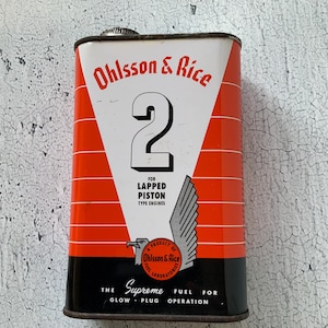 May include: Vintage Ohlsson & Rice fuel can. The can features a white triangle with the number 2, red and black stripes, and text that reads "FOR LAPPED PISTON TYPE ENGINES" and "THE SUPREME FUEL FOR GLOW-PLUG OPERATION."