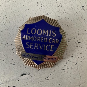 Puede incluir: Una insignia vintage del servicio de coches blindados Loomis. La insignia presenta un escudo azul con letras doradas y un borde dorado. El texto "Safety with Dispatch" se muestra en una pancarta dorada.