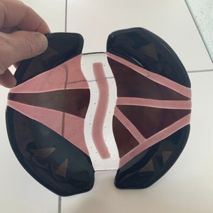 May include: A decorative glass plate with a geometric design. The plate is made of black, white and pink glass. The plate is split into two halves, with a clear glass section in the middle.
