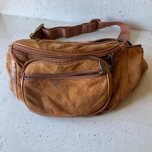Puede incluir: Un bolso de cintura de ante marrón con múltiples compartimentos con cremallera y una correa ajustable. El bolso presenta un bolsillo frontal y un diseño cosido, que ofrece una estética vintage. El bolso de cintura está diseñado para llevar lo esencial.
