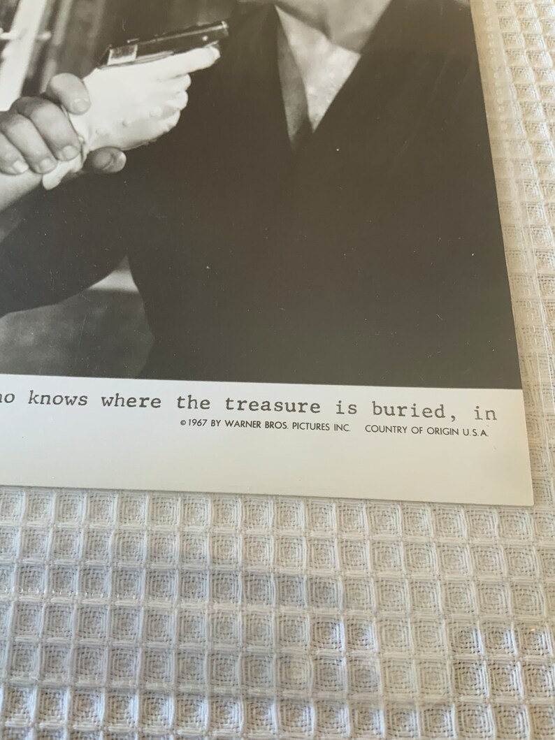 May include: A black and white photo of a man holding a gun. The text below the image reads "no knows where the treasure is buried, in 1967 BY WARNER BROS. PICTURES INC. COUNTRY OF ORIGIN U.S.A."