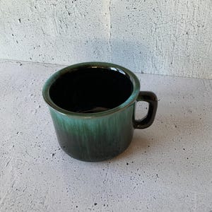May include: A black and green ceramic mug with a handle. The mug has a glazed finish and a dark green color that fades to black.