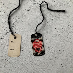 May include: A vintage No. 2 Burgess Uni-Cel Flashlight Battery tag with a black and red design. The tag is attached to a blank price tag with a black string. The battery tag has a shield logo and the text "No. 2".