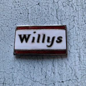 Può includere: Uno spillo in smalto rosso e bianco con la parola "Willys" in lettere nere.