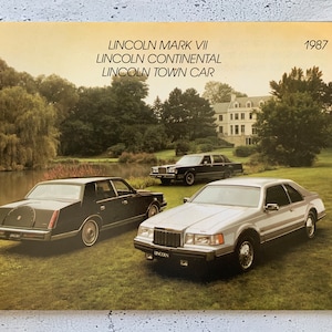 Może przedstawiać: Broszura dla pojazdów Lincoln Mark VII, Lincoln Continental i Lincoln Town Car z 1987 roku. Broszura przedstawia trzy samochody w zielonym otoczeniu z jeziorem i dużym domem w tle.