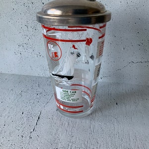 Puede incluir: Un coctelera vintage de vidrio con tapa de plata. La coctelera tiene un diseño de rayas rojas y blancas con una ilustración de un velero. La coctelera tiene una receta para un cóctel Side Car impresa en el lateral: 1/3 de zumo de limón, 1/3 de Cointreau, 1/3 de brandy. Agitar bien con hielo, colar y servir.