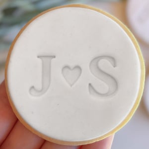 Peut inclure: Un biscuit rond blanc avec les lettres J et S et un symbole de cœur entre les deux.
