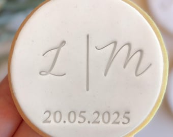 May include: White round cookie with the initials "L | M" and the date "20.05.2025" in gray lettering.