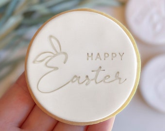 May include: A white round cookie with a gold outline and the words "Happy Easter" and a stylised bunny rabbit design.