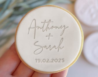 May include: White round cookie with a gold border, decorated with the text "Anthony + Sarah 19.02.2025" in silver lettering.