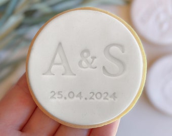 May include: A white round cookie with the letters "A & S" and the date "25.04.2024" embossed on the top.