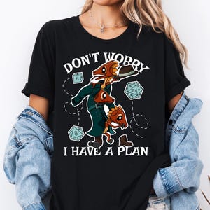 May include: Black t-shirt with a graphic featuring three cartoon dragon-like creatures in a trench coat and hat, with dice and the text "DON'T WORRY I HAVE A PLAN".