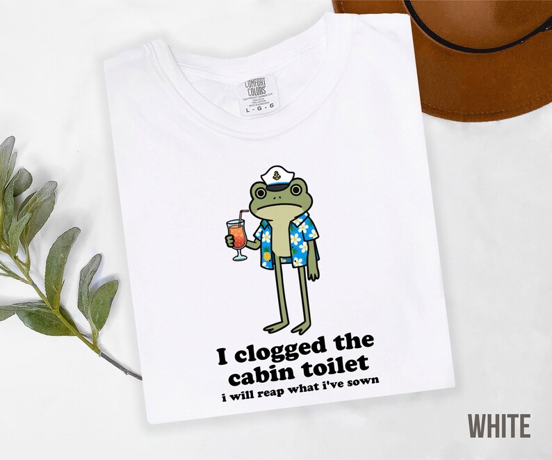 May include: White t-shirt featuring a cartoon frog wearing a captain's hat and Hawaiian shirt, holding a cocktail. Text on the shirt reads "I clogged the cabin toilet, I will reap what I've sown."