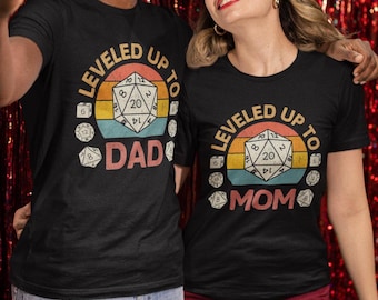 May include: Two black t-shirts with a retro design featuring a 20-sided die and the text "LEVELED UP TO DAD" and "LEVELED UP TO MOM".