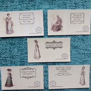 May include: Set of six vintage-style cards featuring illustrations of women in period clothing. Each card has a humorous quote in a decorative frame. The quotes include: "I don't spew profanities. I enunciate them like a lady.", "Damaged but adorable.", "I'm here. I'm awake. Don't push it.", "Don't judge yourself too harshly. Leave that to me.", "You will pry this coffee cup out of my cold, dead hands."