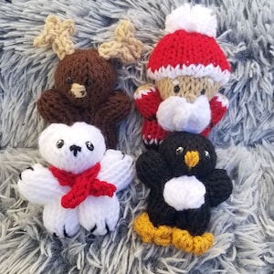 May include: Four knitted Christmas ornaments: a reindeer, Santa Claus, a polar bear, and a penguin. The reindeer is brown with antlers, Santa is wearing a red hat and white beard, the polar bear is white with a red scarf, and the penguin is black and white with yellow feet.