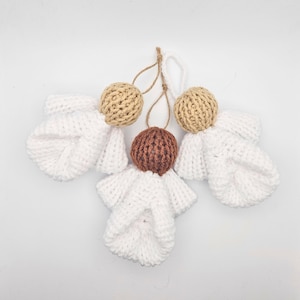 Könnte beinhalten: Drei handgefertigte Engel-Ornamente aus Strick. Jeder Engel hat einen weißen Körper und Flügel, mit einem Kopf aus beigem oder braunem Garn. Die Ornamente sind mit Schnur- oder weißen Garnschleifen aufgehängt.