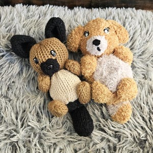 May include: Two knitted stuffed animals, a brown and black dog and a brown and white dog, are lying on a fluffy gray rug.
