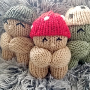 Op de afbeelding: Drie gebreide poppen in de vorm van een paddenstoel met verschillende gekleurde hoeden. De pop links heeft een groene hoed, de pop in het midden heeft een rode hoed met witte stippen en de pop rechts heeft een beige hoed.