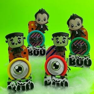 Peut inclure: Quatre boîtes de fête sur le thème d'Halloween avec différents personnages. Chaque boîte présente un personnage différent : un vampire, un Frankenstein et deux autres vampires. Les boîtes sont décorées de motifs colorés et du mot « BOO » en lettres noires.