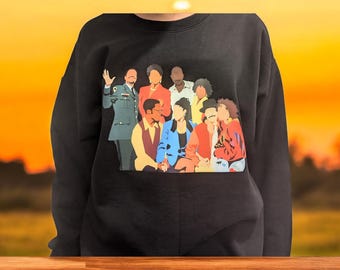Op de afbeelding: Zwart sweatshirt met een kleurrijke grafische print van een groep mensen. De print bevat een verscheidenheid aan kleuren, waaronder rood, blauw, groen, geel en zwart.