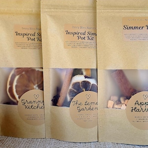May include: Four stand-up kraft paper pouches labeled Simmer Pot Kit with clear windows displaying dried fruit and spices. Labels include names like Apple Harvest, The Lemon Garden, Granny's Kitchen, and Mulling Aroma, with pumpkins on the sides.