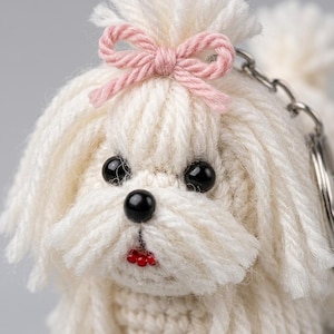 Puede incluir: Un llavero de ganchillo con forma de perro pequeño blanco con pelo de lana largo, que presenta un lazo de lana rosa claro en la parte superior de la cabeza, dos ojos de cuentas negras, una nariz de cuenta negra y una boca de cuenta roja.