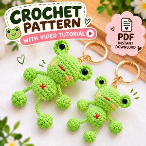 May include: Two light green crocheted frog keychains with black eyes, pink cheeks, and a red cross on the belly. The image includes text: CROCHET PATTERN WITH VIDEO TUTORIAL and PDF INSTANT DOWNLOAD. The frogs have gold-colored metal key rings.