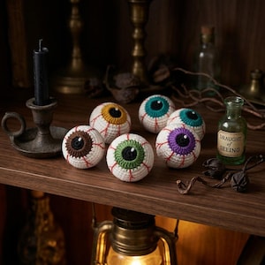 Può includere: Sei bulbi oculari sferici all'uncinetto con sclera bianca e vene rosse ricamate. Ogni occhio presenta un colore dell'iride distinto: marrone, giallo, verde, viola e due tonalità di verde acqua. È presente una boccetta con etichetta Draught of Seeing.