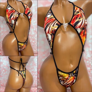May include: A one-piece swimsuit featuring a vibrant red, orange, and black abstract butterfly wing pattern. The garment includes a halter neckline, thin black straps, and a central silver-toned rhinestone embellishment at the chest.