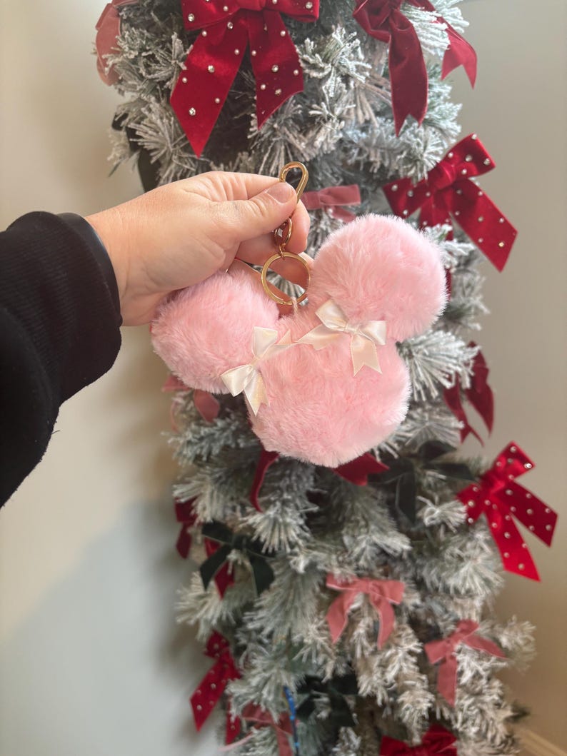 May include: Pink fuzzy keychain with a gold ring and two white bows. The keychain is shaped like a mouse head.