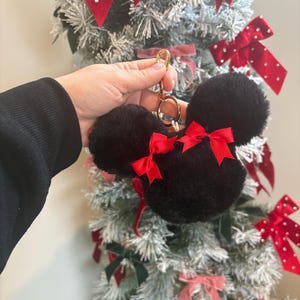 May include: Black fuzzy keychain with red bows shaped like Mickey Mouse ears. The keychain is attached to a gold ring.