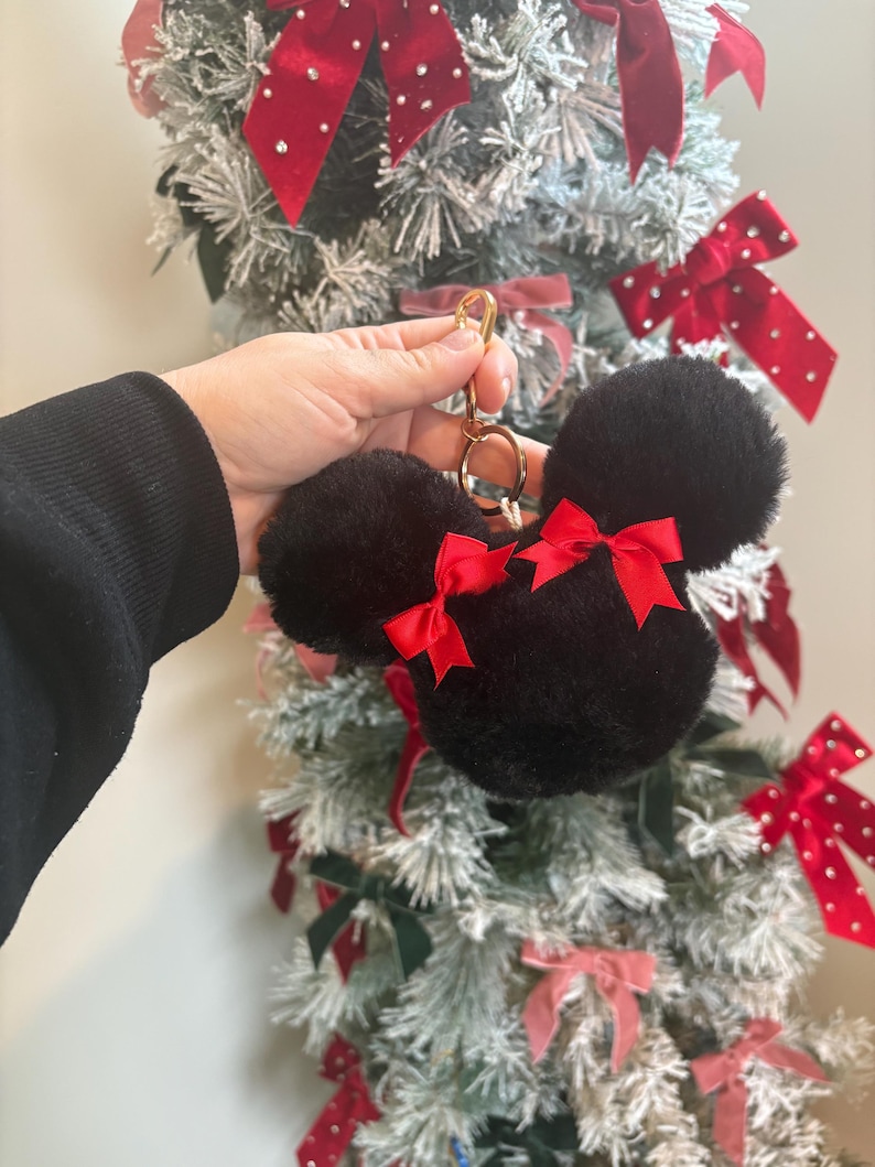 May include: Black fuzzy keychain with red bows shaped like Mickey Mouse ears. The keychain is attached to a gold ring.