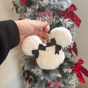 May include: White fluffy keychain with black bows shaped like Mickey Mouse ears. The keychain is attached to a gold key ring.