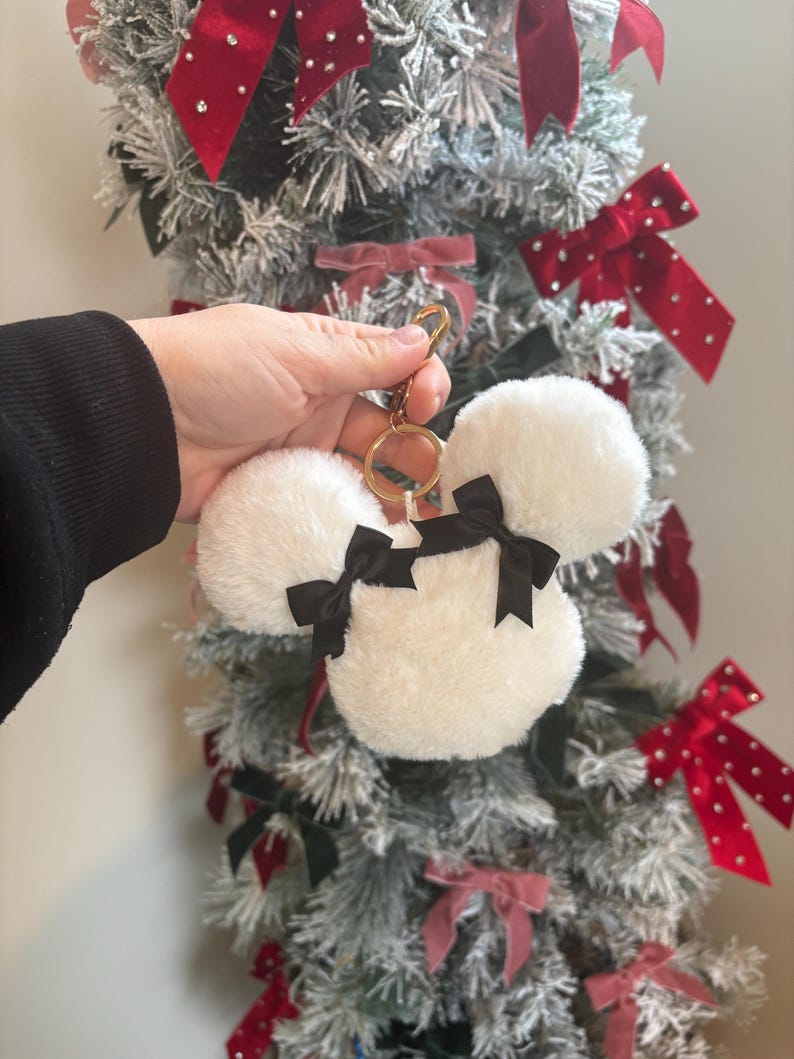 May include: White fluffy keychain with black bows shaped like Mickey Mouse ears. The keychain is attached to a gold key ring.