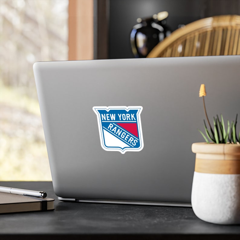 Op de afbeelding: Een blauwe en rode sticker met het logo van het New York Rangers hockeyteam op een zilveren laptop.