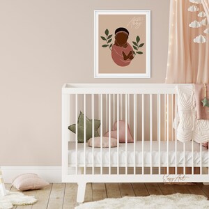 Op de afbeelding: Een wit babybedje met een wit matras en een roze-wit dekentje. Er ligt een groen-wit kussen in de vorm van een ster in het bedje. Een ingelijst printje met een baby met een bruine huid in een roze outfit en groene bladeren hangt aan de muur achter het bedje. De print heeft de naam "Aaliyah" erop staan.