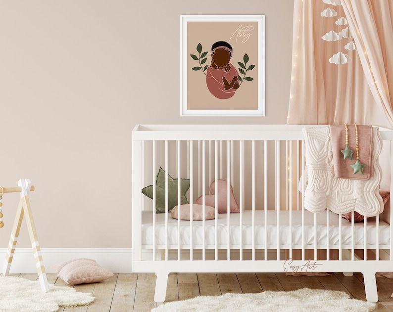 Op de afbeelding: Een wit babybedje met een wit matras en een roze-wit dekentje. Er ligt een groen-wit kussen in de vorm van een ster in het bedje. Een ingelijst printje met een baby met een bruine huid in een roze outfit en groene bladeren hangt aan de muur achter het bedje. De print heeft de naam "Aaliyah" erop staan.