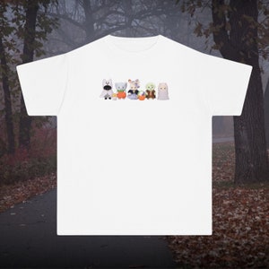 May include: White t-shirt with a graphic of six cartoon characters dressed in Halloween costumes. The characters are holding pumpkins and candy.