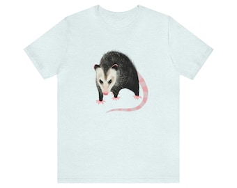 Pode incluir: Uma camiseta azul claro com uma ilustração em preto e branco de um gambá com uma cauda rosa.