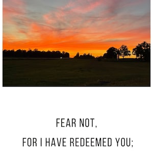 May include: A sunset sky with a field in the foreground. The sky is a vibrant orange and pink with clouds. The text "FEAR NOT, FOR I HAVE REDEEMED YOU; I HAVE SUMMONED YOU BY NAME; YOU ARE MINE. Isaiah 43" is written in black text on a white background.