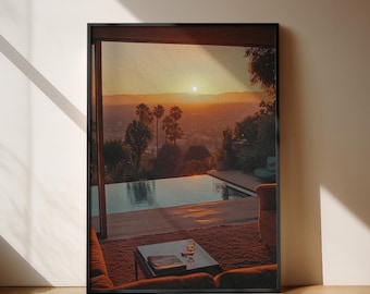 May include: A framed photograph of a sunset over a city with a swimming pool in the foreground. The pool is surrounded by a patio with a couch and a coffee table.